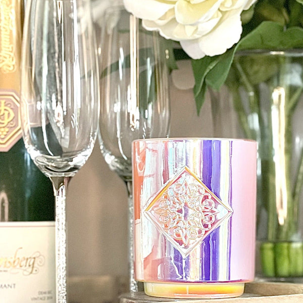 Load image into Gallery viewer, Iridescent white holographic glass with custom intricate logo inside a diamond depression. The base is smaller than the top of the candle. This candle smells like coconut and woody santal.