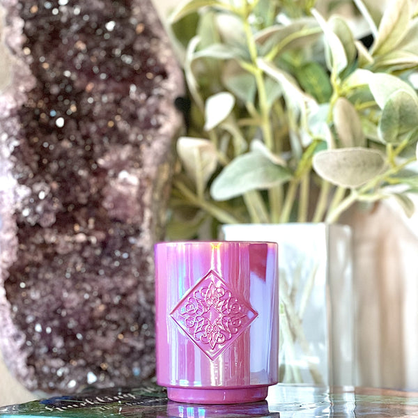 Load image into Gallery viewer, Iridescent purple glass with custom intricate logo inside a diamond depression. The base is smaller than the top of the candle. This candle smells like blooming French lilac and white tea.
