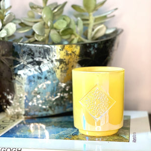Iridescent yellow glass with custom intricate logo inside a diamond depression. The base is smaller than the top of the candle. This candle smells like blooming white jasmine and bergamot flowers.